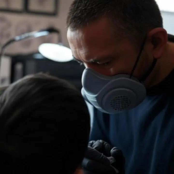 Tetoválóművész koncentráltan dolgozik egy vendég karján a stúdióban